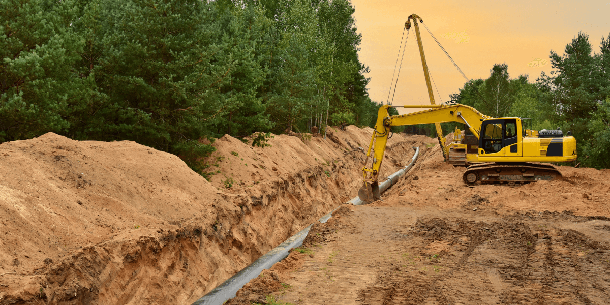 An excavator laying a pipeline in a freshly dug trench